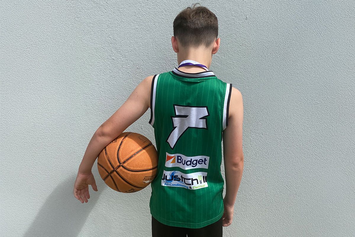 Young basketball player wearing a jersey with Just Chill logo, holding a basketball.